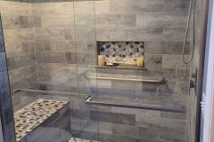 Picture of a custom shower, glass barndoor style walk in feature, stone tile on floor and as accents. Rainforest showerhead and detachable by Martin Construction Services